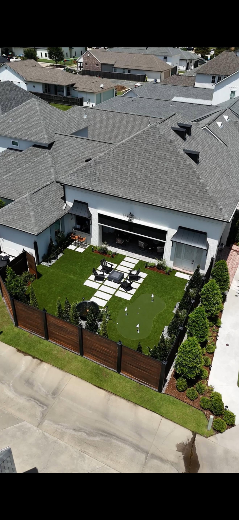 Aerial view of a landscaped backyard with a putting green, patio seating, and planting beds.